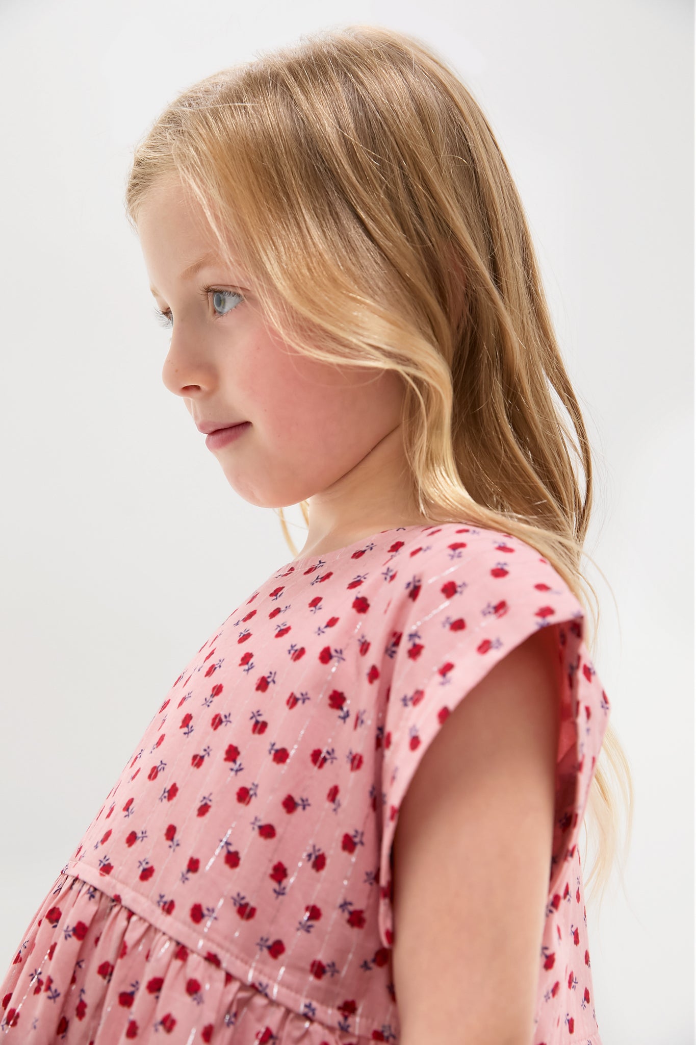 Young girl in profile wearing the classic Girls Peachy Dress, featuring an effortless pink floral pattern, triple-tiered silhouette, and cap sleeves for a fun, high-end look.