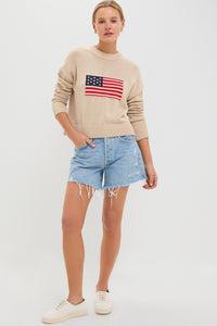 A woman wears a Tuckernuck Cropped Americana Sweater with an intarsia flag, distressed denim shorts, and white sneakers. The sweater’s boxy fit gives her casual look a modern edge.