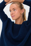 Young woman wearing the classic Navy Cable Ally Swing Sweatshirt, showcasing its effortless style with a cable texture, drop shoulders, and three-quarter sleeves, paired with a polished gold earring.