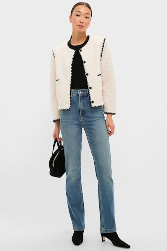 Woman models Cream & Black Trim Sherpa Audrey Jacket with black top, blue jeans, and black ankle boots, embodying classic, effortless style with a high-end, fun appeal.