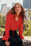 A woman sits on a city park bridge wearing a red blouse and back pants.