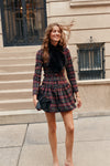 A woman wearing a tartan patterned mini dress and a brown fur scarf carries a black tassel clutch.