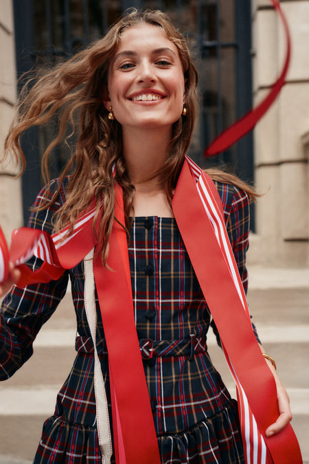 A woman wearing a tartan patterned mini dress with red and white striped ribbon around her shoulders.
