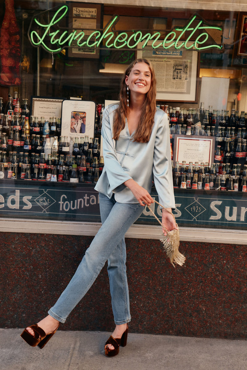 Young woman in an Ice Blue Satin Tatiana Blouse with a V-neckline and frog closures, embodying classic, effortless style; perfect for fun, high-end day-to-night looks.