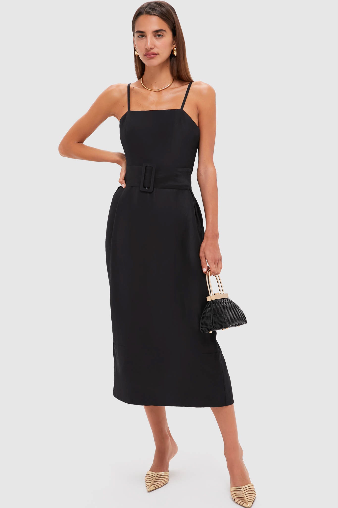 Model in a classic Black Artichoke Dress with Belt, paired with an effortless woven handbag and fun gold mules, embodying a high-end, confident style.
