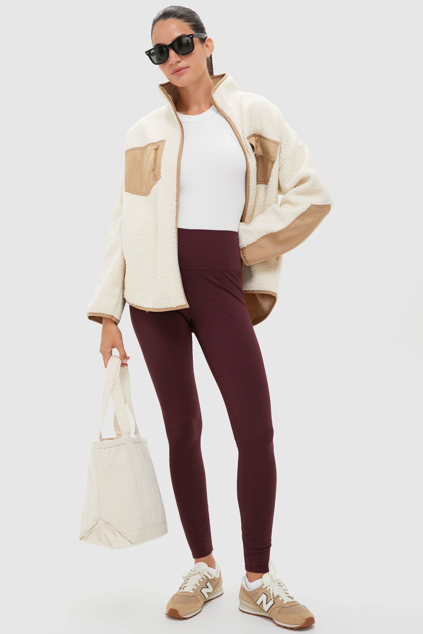 Model wearing the Buttercream Fleece Lawrence Full Length Zip Up, a classic sherpa jacket with contrast trim, paired effortlessly with burgundy leggings and canvas tote for a high-end, fun look.