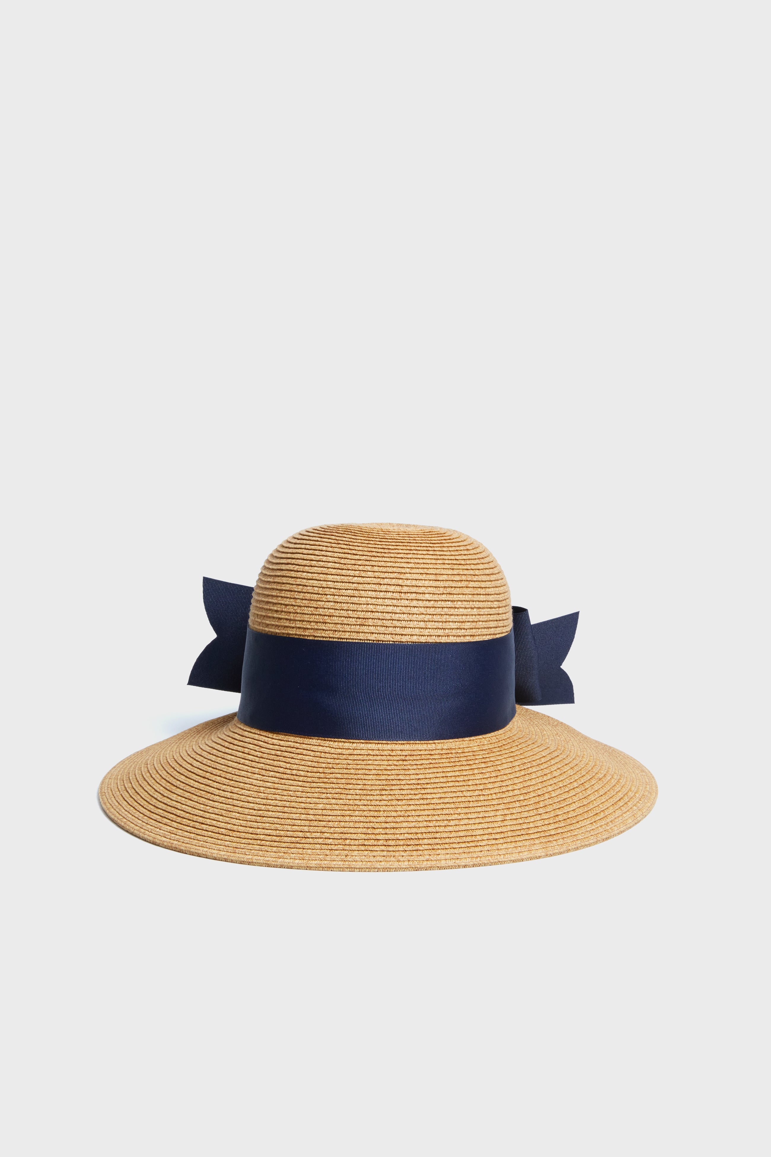 The Toucan Hats wide brim straw hat features a dark blue ribbon bow around the crown, making it a perfect navy bow sun hat for sunny days.