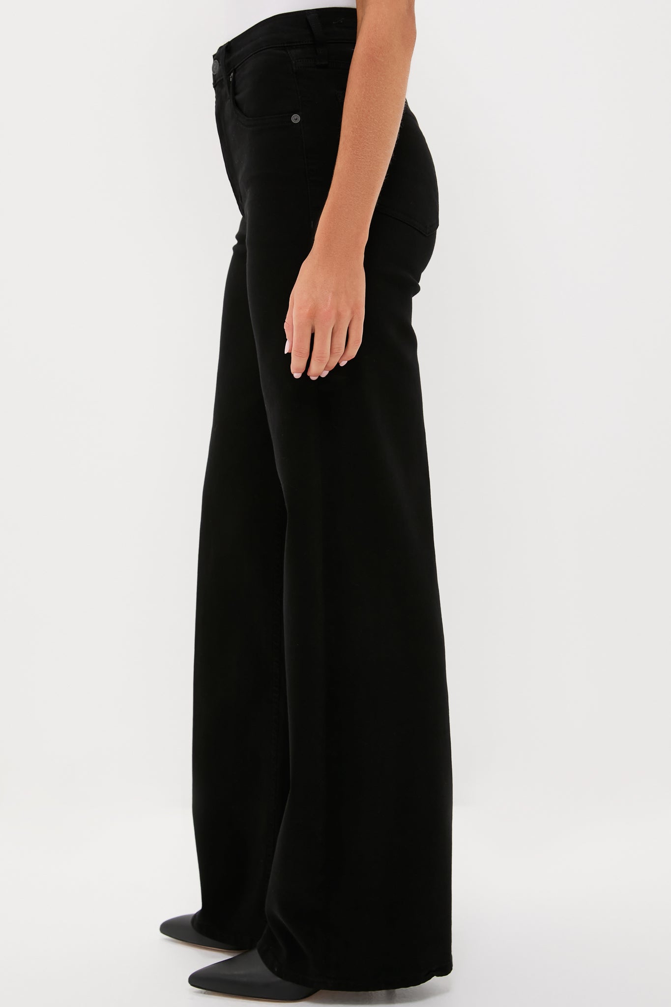 A person in Citizens of Humanity high-rise wide leg jeans and pointed black shoes stands against a plain white background.