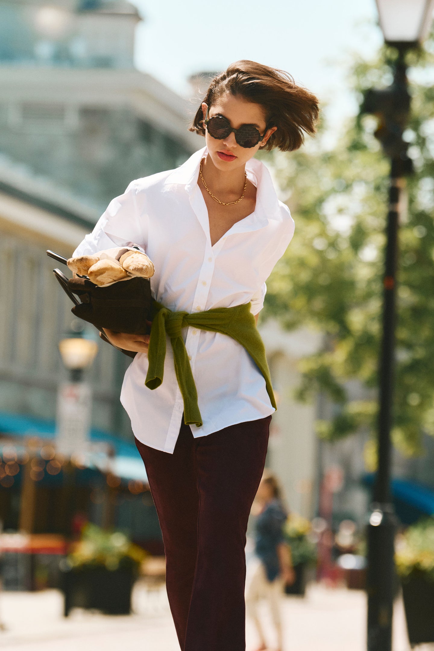 Woman in a white button down and burgundy pants with a green sweater wrapped around her waist. 