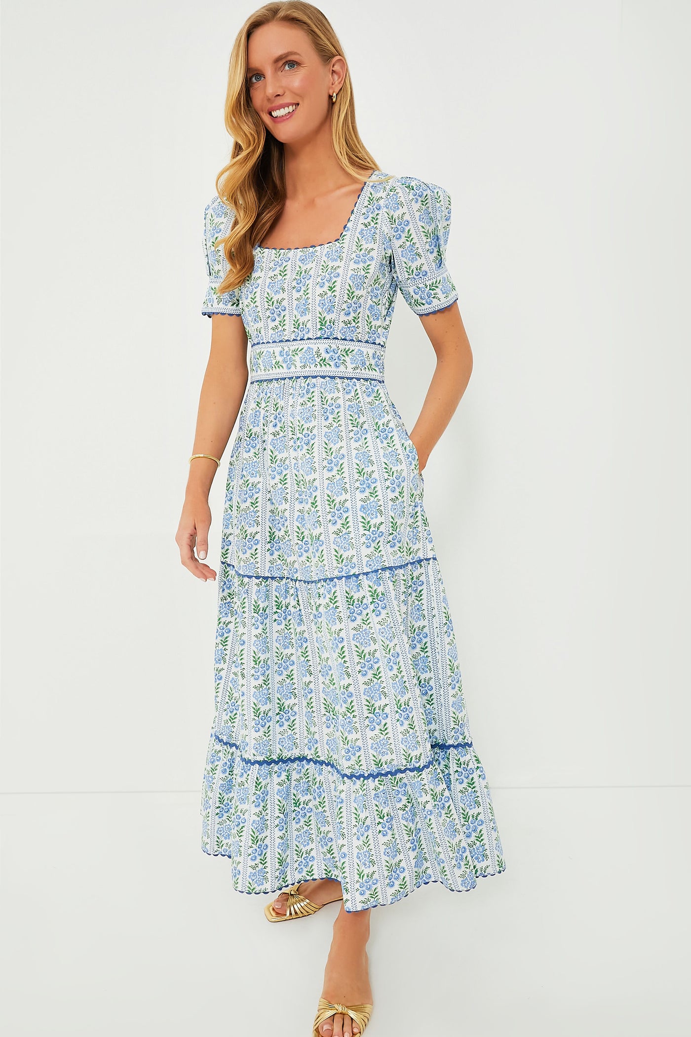 A woman wears a Pink City Prints blue and white floral organic cotton dress with short puff sleeves and a square neckline, highlighting sustainable fashion.