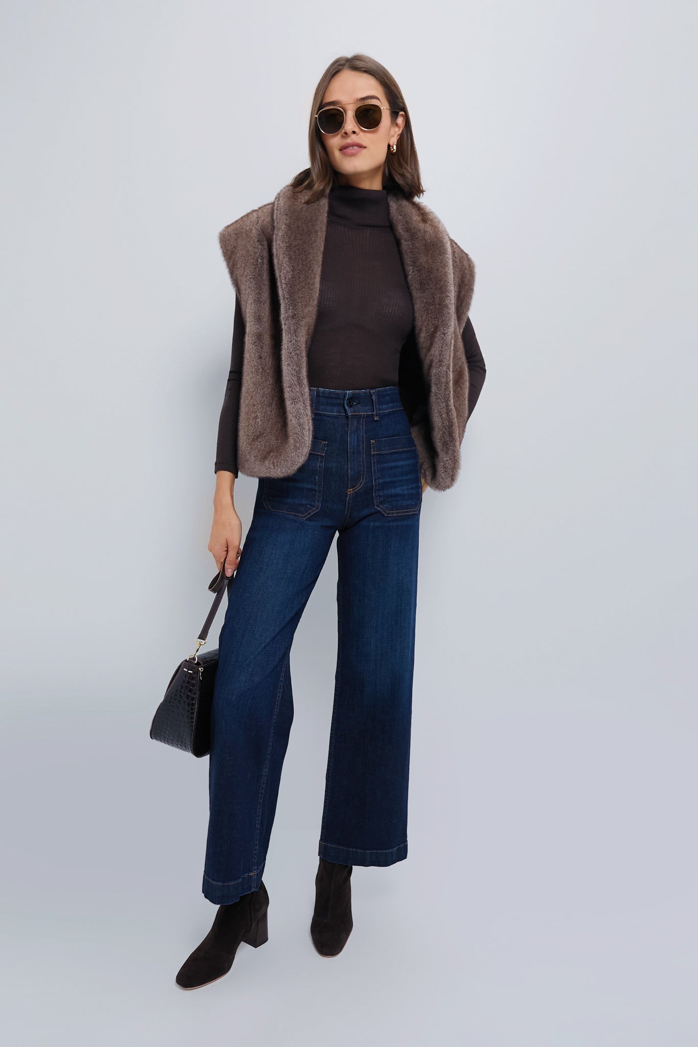 Woman in a classic, oversized Aspen Faux Fur Vest, exuding effortless style with black turtleneck, wide-leg jeans, and high-end accessories, epitomizing fun, chic fashion.