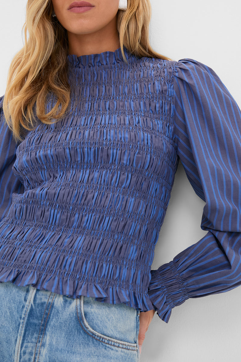 Morgan Blue Willow Top exudes classic elegance with its high ruffle collar, breezy balloon sleeves, and smocked bodice, paired effortlessly with light-wash jeans.