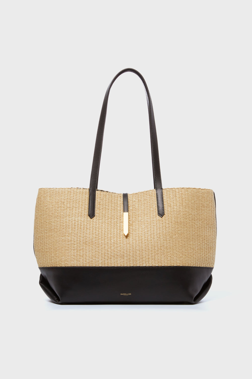 The Demellier woven raffia tote features a beige and black design, two dark handles, and a gold accent, highlighting the brand’s elegant handcrafted style.