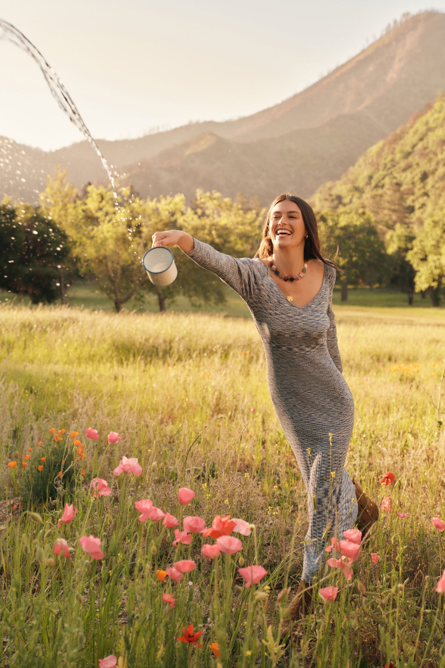 Woman throwing water out of a mug in blue long sleeved maxi sweater dress. 