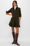 A woman stands with one hand on her hip, wearing a relaxed fit Tuckernuck Callahan Shirt Dress in dark olive over a white turtleneck and tall brown boots.