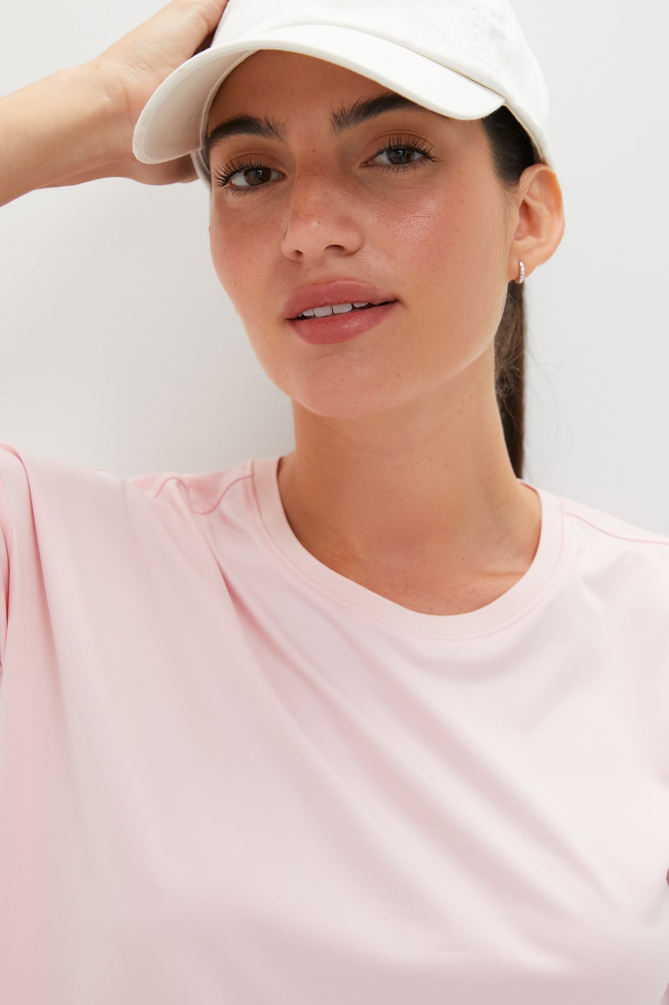 Young woman in a classic, effortless Pink Long Sleeve Performance Jersey Ryan Boyfriend Tee, showcasing fun, high-end style with a white baseball cap and small hoop earring.