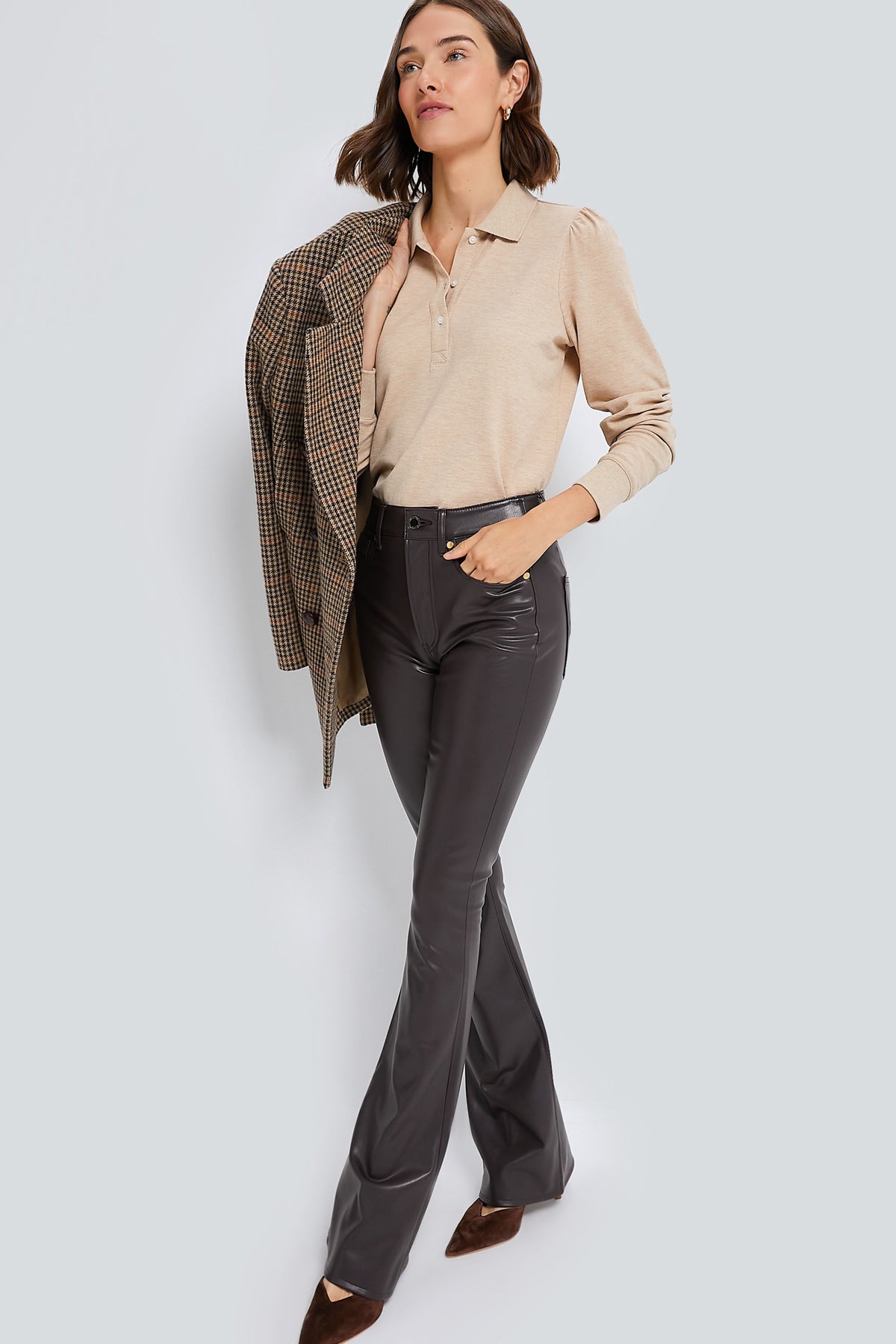 A woman wears a Tuckernuck beige long-sleeve top with a ribbed collar, dark flared pants, brown pointed shoes, and holds a checkered blazer over her shoulder.