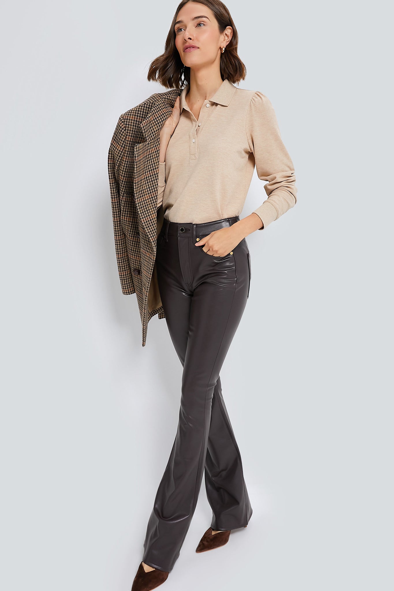 A woman wears a Tuckernuck beige long-sleeve top with a ribbed collar, dark flared pants, brown pointed shoes, and holds a checkered blazer over her shoulder.