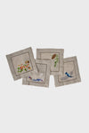 Set of four Juliska hand-embroidered linen cocktail napkins featuring nature-inspired designs—a bird, flowers, pinecone, and leaves—with elegant style.
