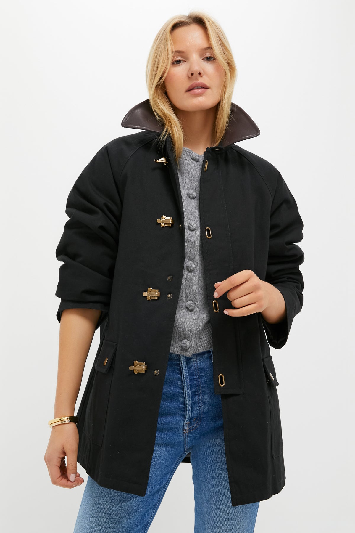 A woman models a Tuckernuck Black Barn Jacket with a popped faux leather collar, gray buttoned shirt, and blue jeans against a white background.