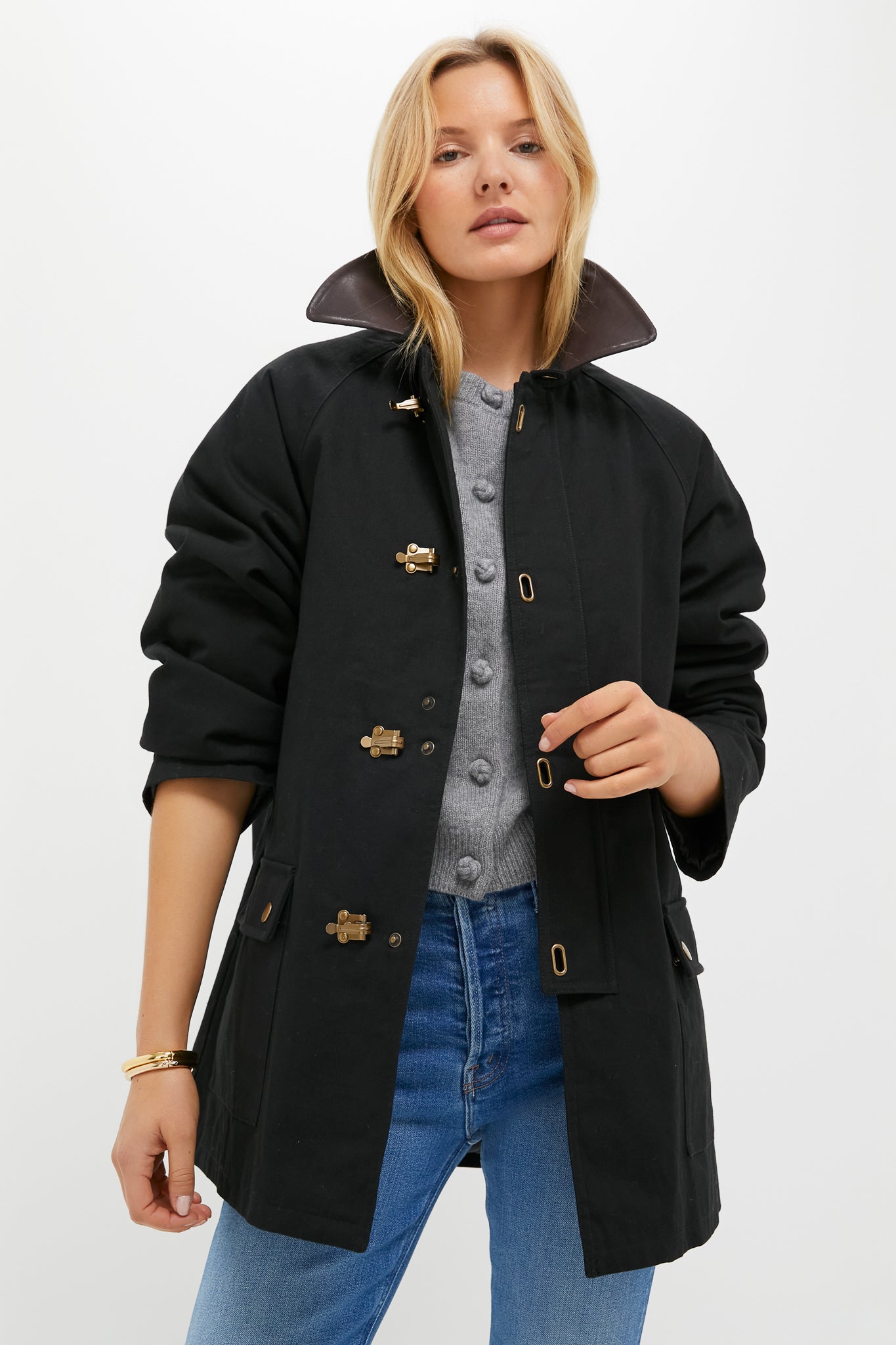 A woman models a Tuckernuck Black Barn Jacket with a popped faux leather collar, gray buttoned shirt, and blue jeans against a white background.