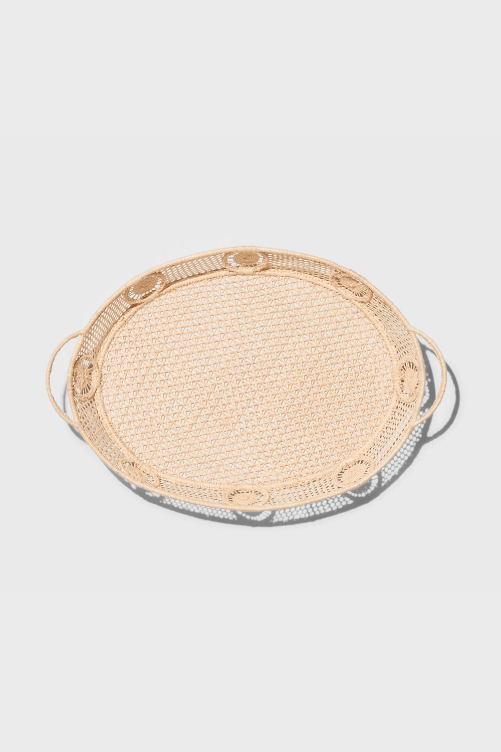 The AERIN round rattan tray features two side handles and raffia accents, adding a touch of coastal design.