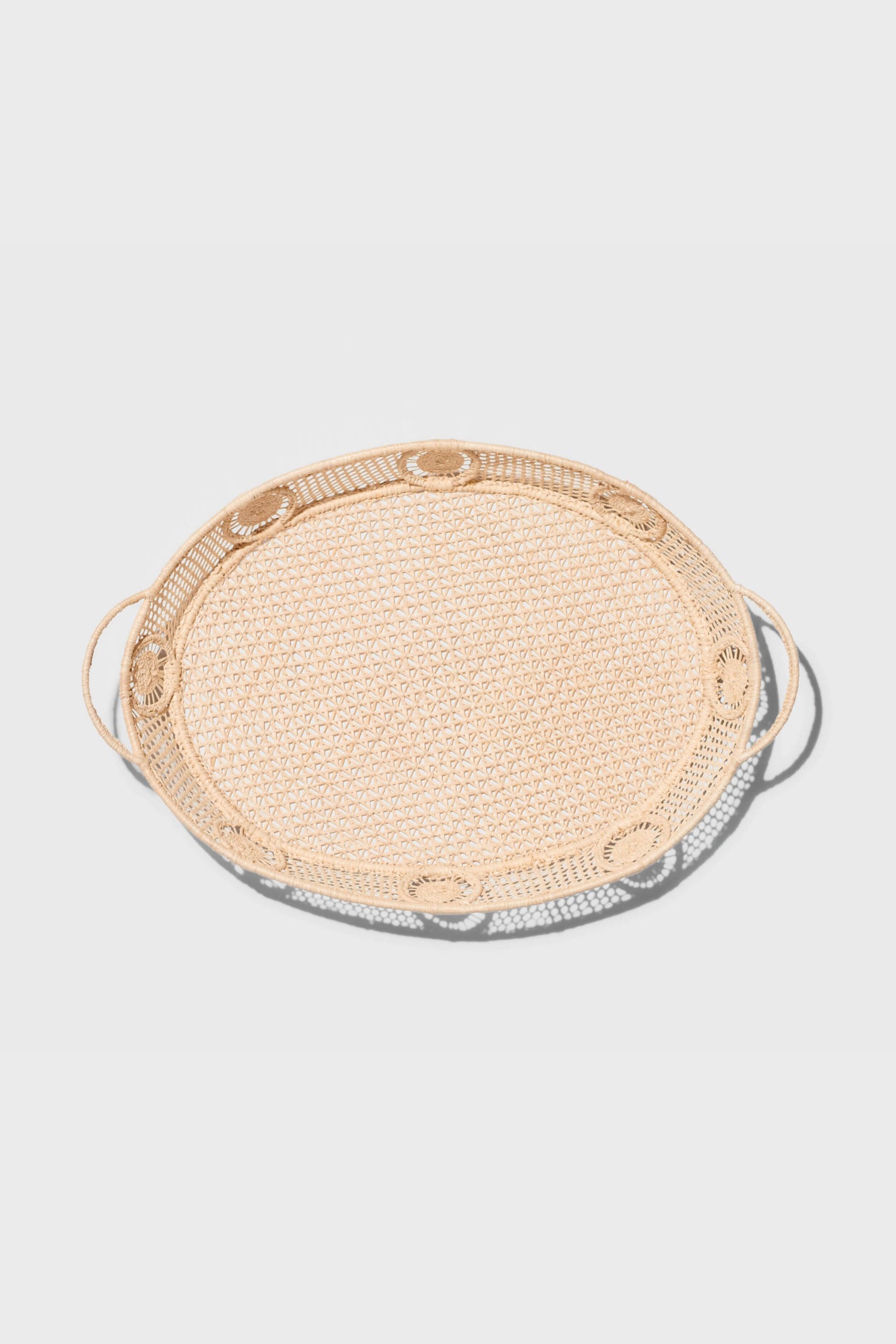 The AERIN round rattan tray features two side handles and raffia accents, adding a touch of coastal design.