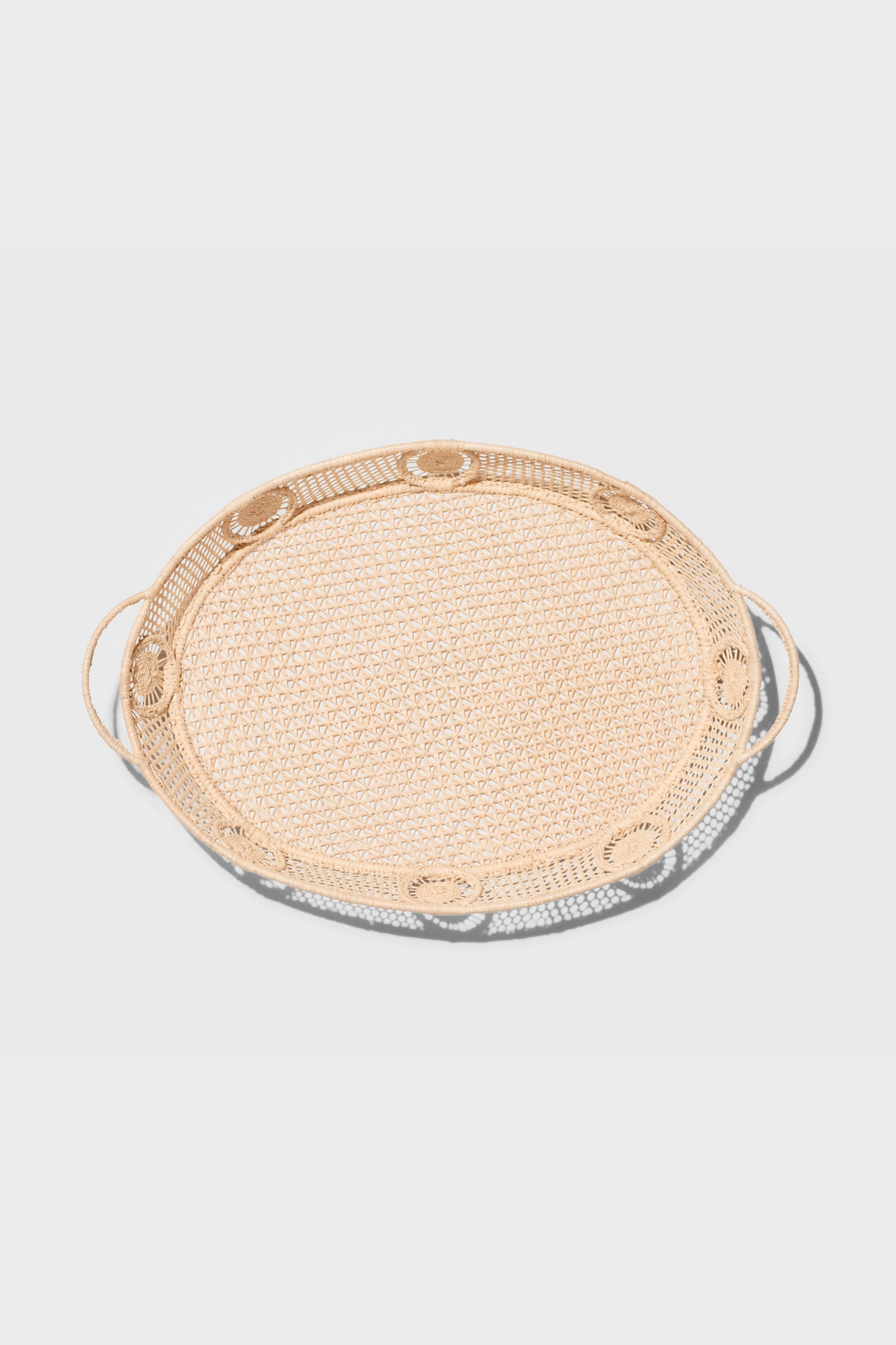 The AERIN round rattan tray features two side handles and raffia accents, adding a touch of coastal design.