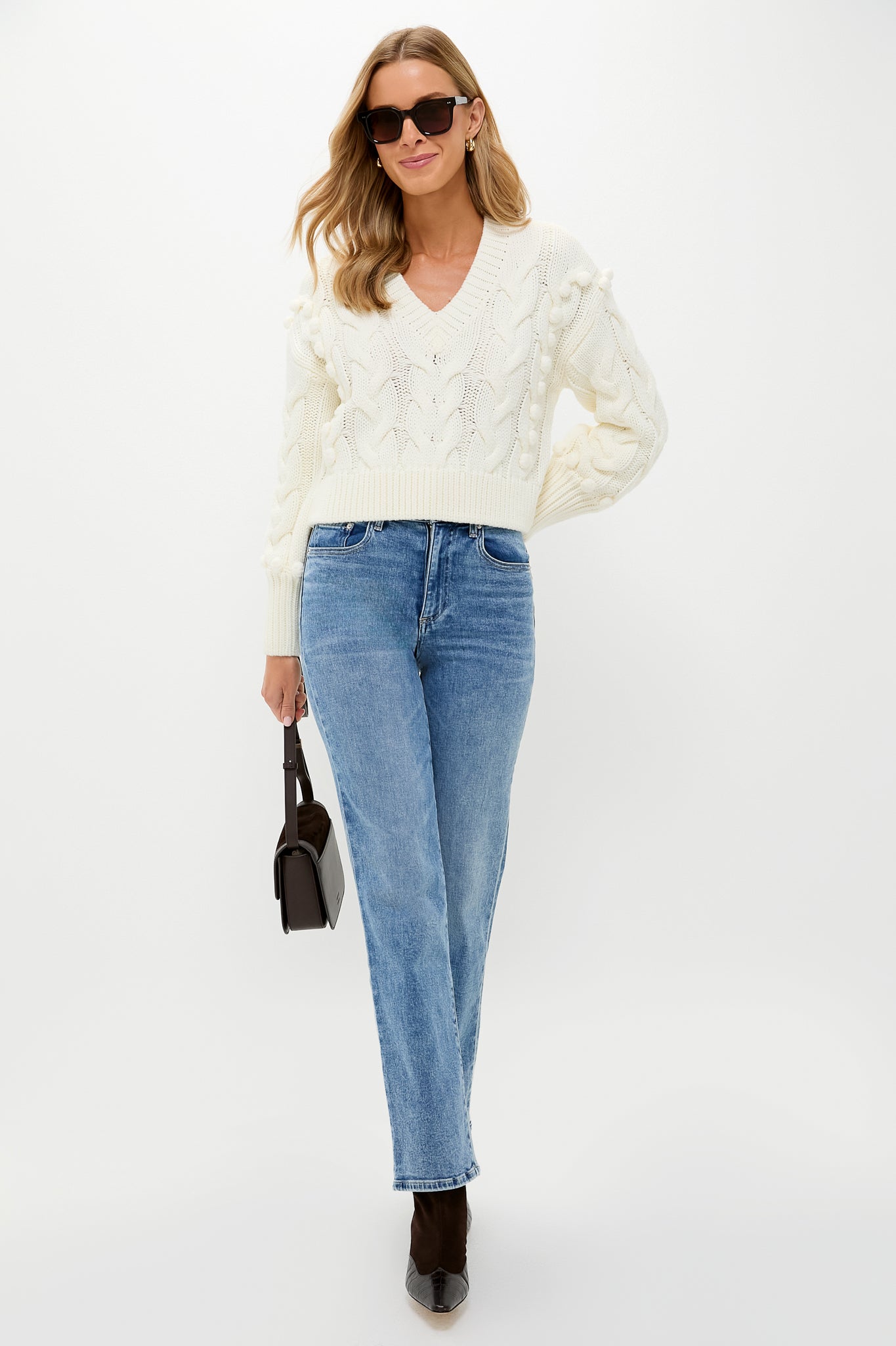 Woman models the Ivory Cable Knit Cropped Contessa V-Neck Sweater, showcasing its classic, effortless style with a fun, high-end edge, perfect for versatile, chic outfits.