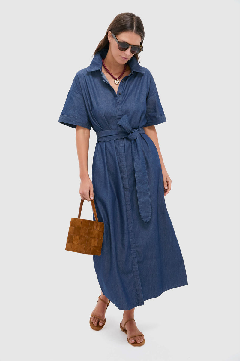 Model wearing the classic Dark Denim Zacara Dress with effortless style, featuring a self-tie belt and drop shoulders, accessorized with a brown suede tote and sandals.