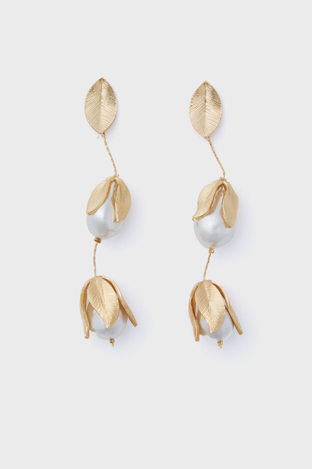 The Gold Falcao Earrings by Petit Moments are gold-tone drop earrings with textured leaf shapes and pearl-like beads, crafted in a chic vertical design.