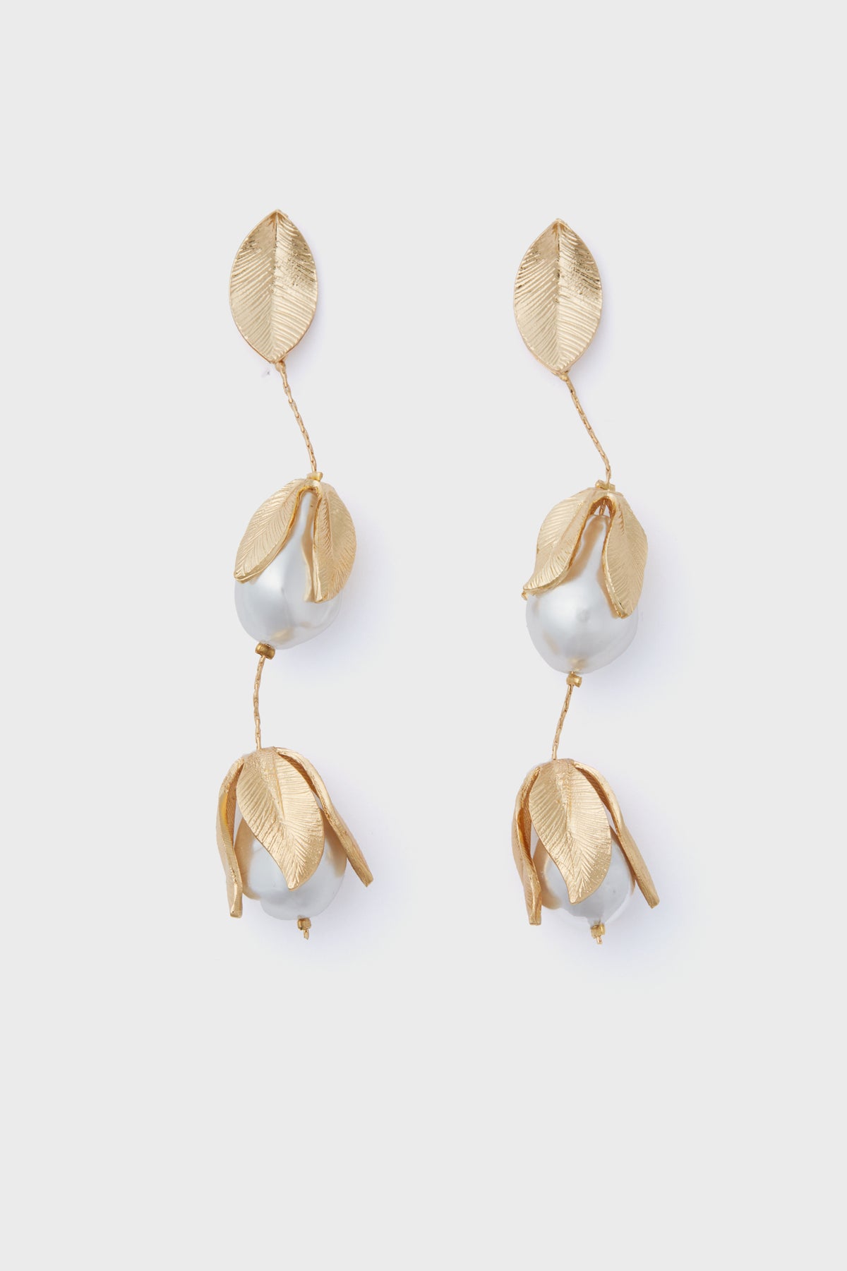 The Gold Falcao Earrings by Petit Moments are gold-tone drop earrings with textured leaf shapes and pearl-like beads, crafted in a chic vertical design.