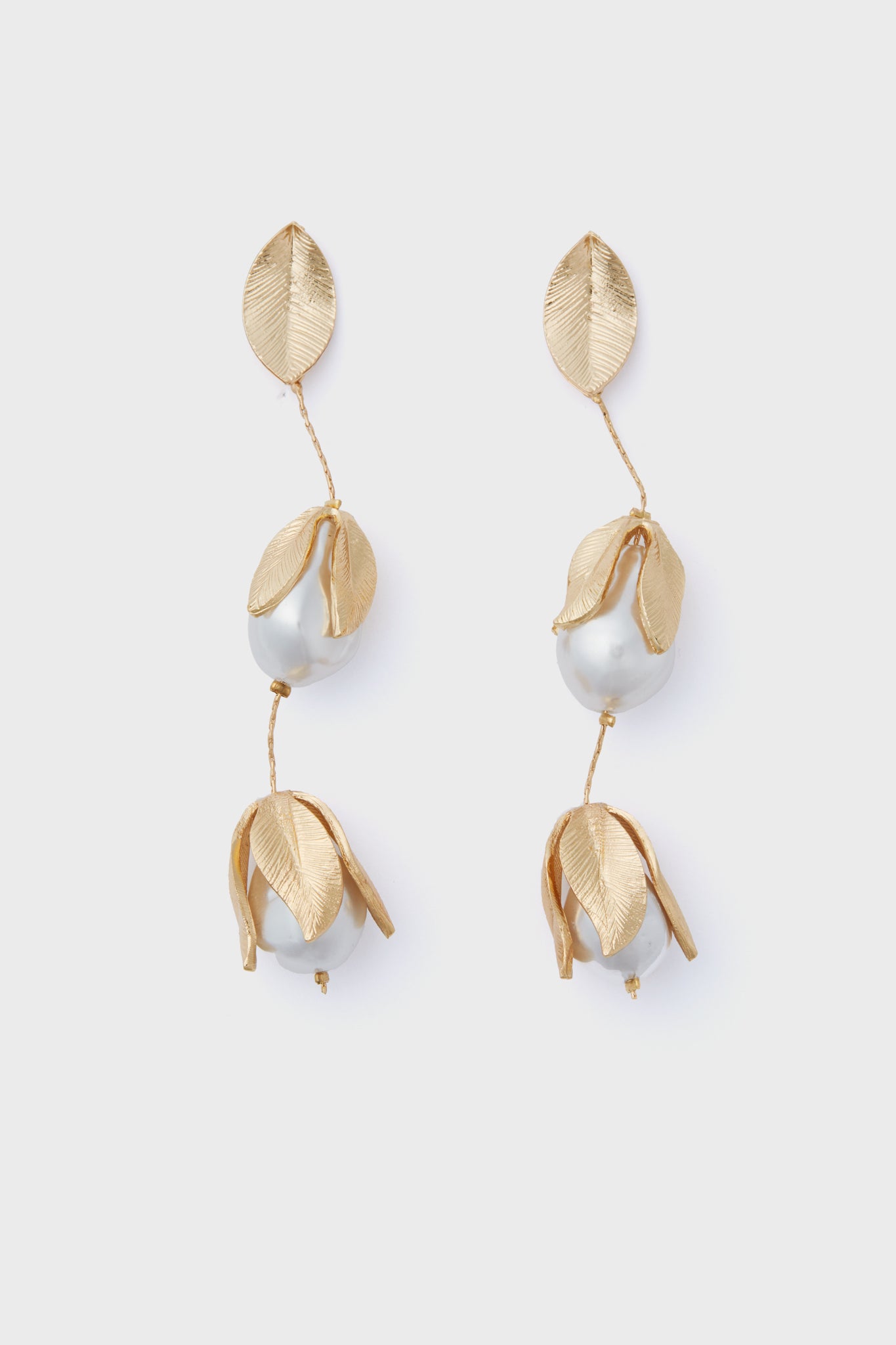 The Gold Falcao Earrings by Petit Moments are gold-tone drop earrings with textured leaf shapes and pearl-like beads, crafted in a chic vertical design.