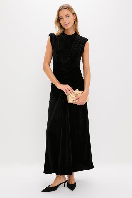 A woman in a Saylor sleeveless black floor-length dress, black pointed heels, and holding a gold clutch stands against a plain white background.