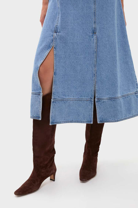 A person in a Hunter Bell blue denim midi dress with front slits, styled with knee-high dark brown suede boots.