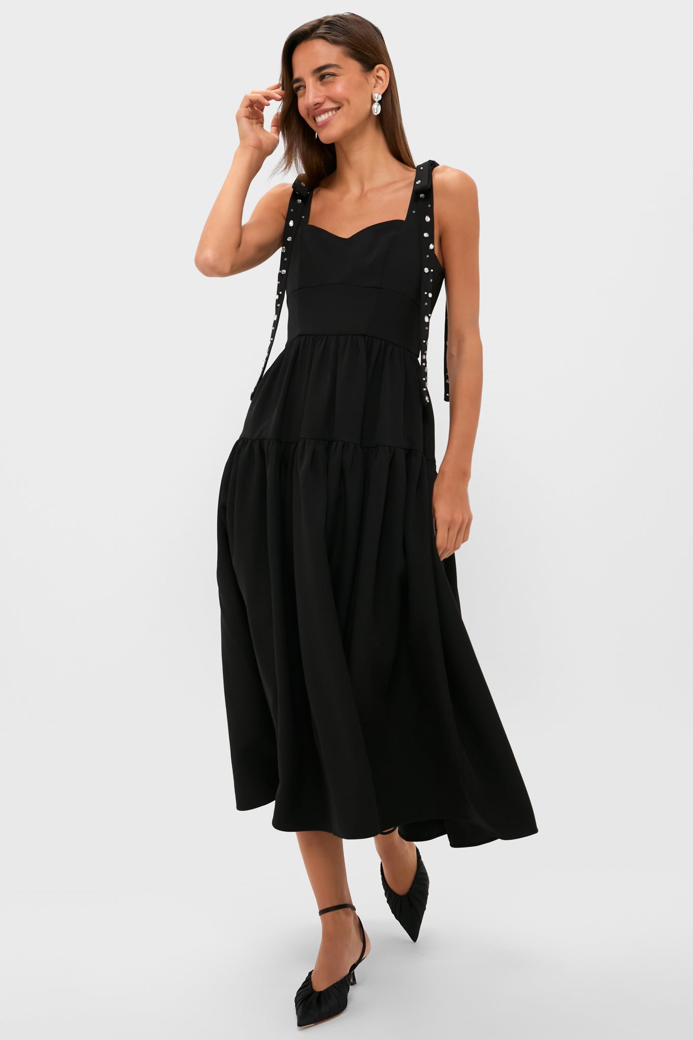 A woman wears a Hyacinth House sleeveless little black dress with ribbon tie straps and black pointed-toe heels, exuding evening glamour.