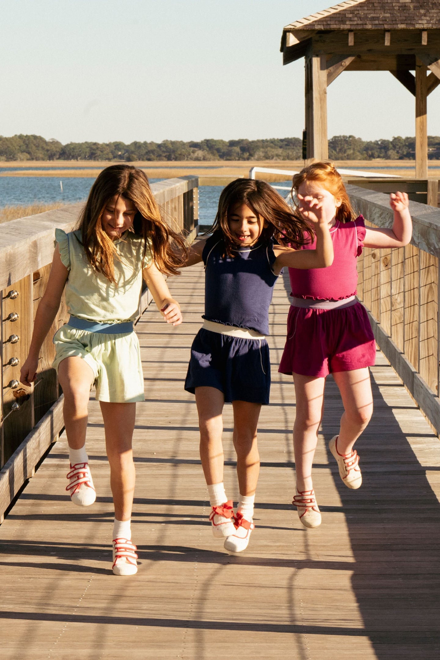 Three little girls jumping in the air wearing matching sets in yellow, blue, and red. 