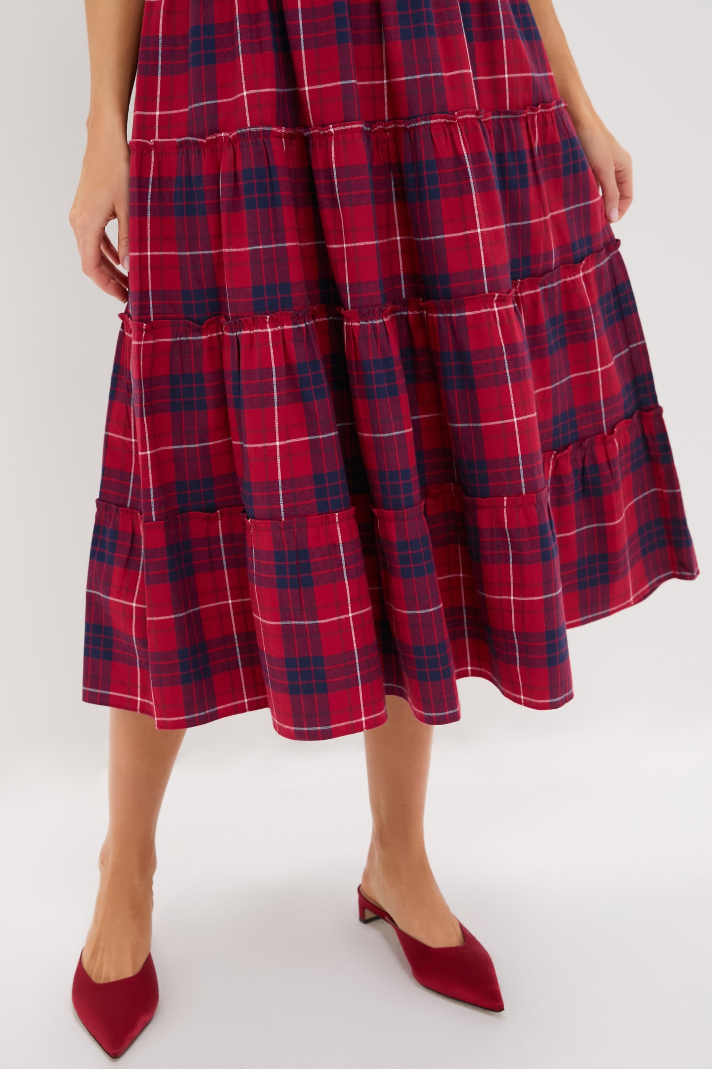 A person wearing a Hill House Home red and navy plaid A-line midi skirt with red pointed low-heeled shoes stands against a plain background.