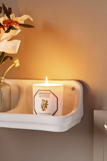 Classic white wall-mounted shelf with an effortless touch: Blossom Candle by Carrière Frères, paired with a textured vase of lily and berries, creating a high-end, fun ambiance.