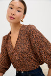 A woman in a Pomander Place leopard print top with puffed sleeves and gold hoop earrings sits against a plain background.