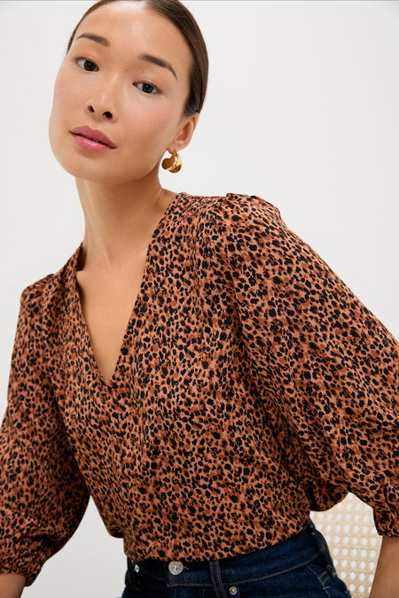 A woman in a Pomander Place leopard print top with puffed sleeves and gold hoop earrings sits against a plain background.