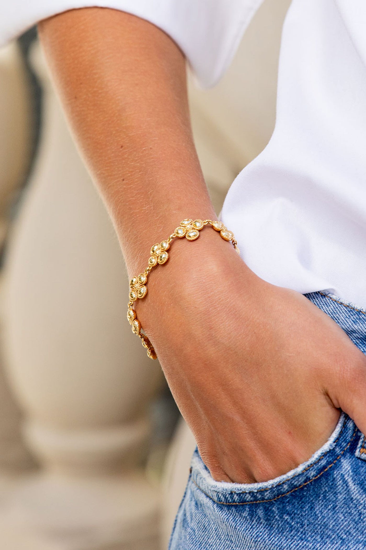 Classic and effortless, the Berry Clover Linear Bracelet in gold adorns a wrist, adding a touch of fun and high-end charm against casual denim.