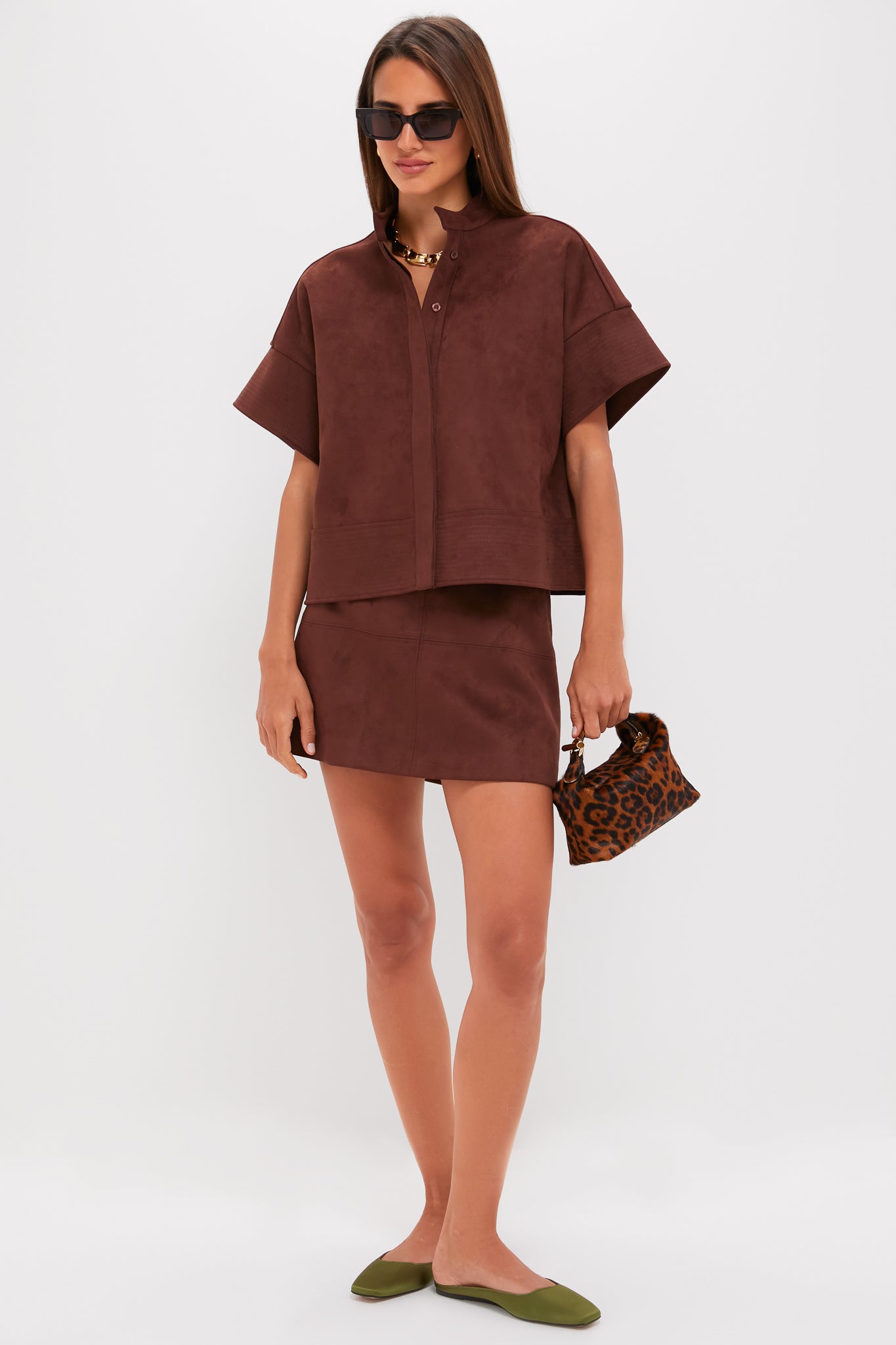 Model showcases the classic Ganache Vegan Suede Meg Mini Skirt, an effortless high-end piece paired with a matching top and fun accessories, embodying chic style.