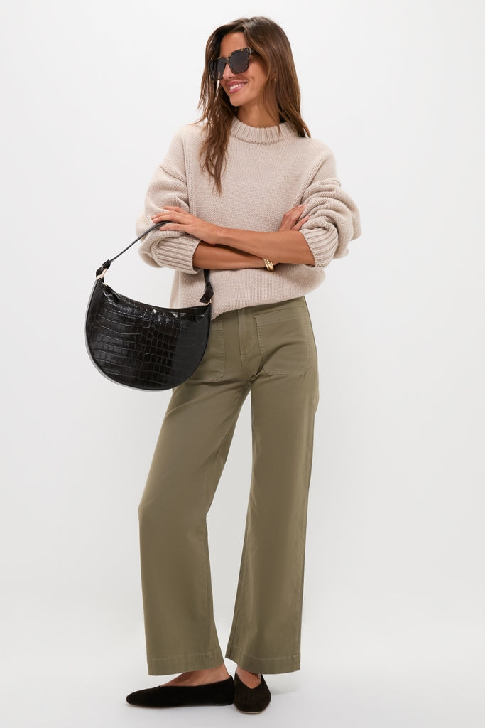 Woman in an oatmeal sweater and Olive Sailor Pant, embodying classic, effortless style. The high-end wide-leg trousers pair seamlessly with her chic accessories, exuding fun sophistication.