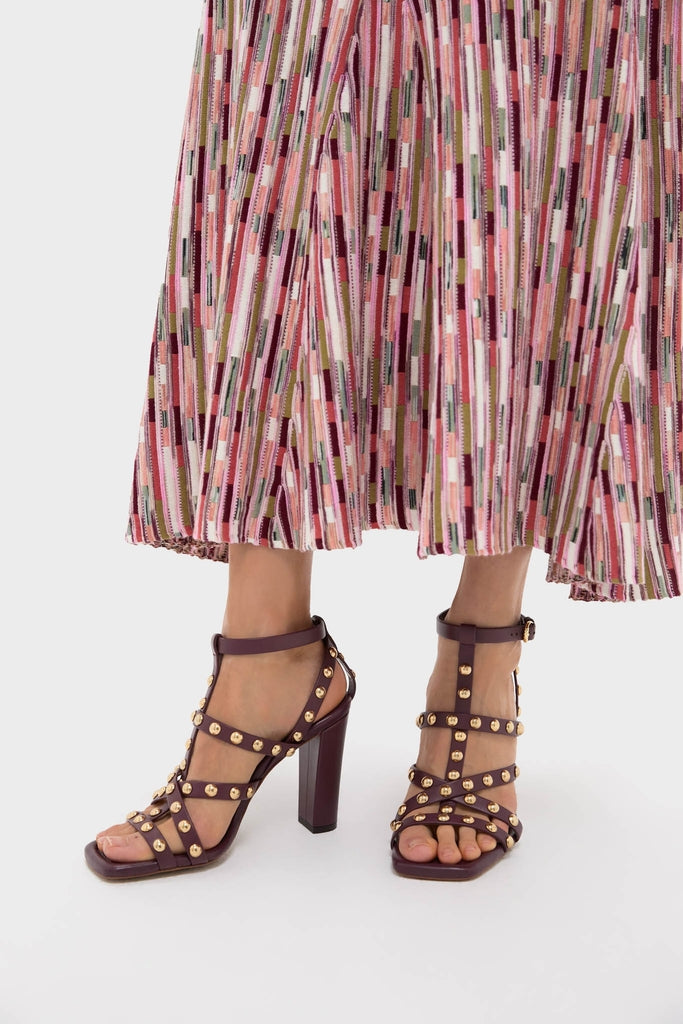 Cognac Studded Cage Heels with classic T-strap design, dark burgundy tone, and gold studs, paired effortlessly with a pleated multicolored striped midi skirt.