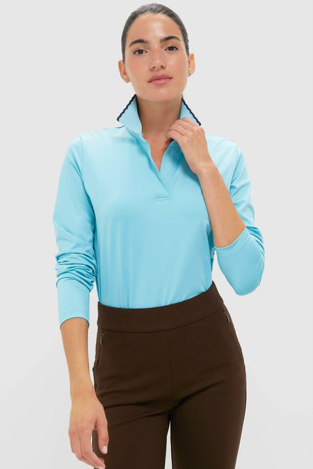 A woman confidently stands wearing a Tnuck Sport light blue quick-dry performance long-sleeve collared shirt and dark brown pants.