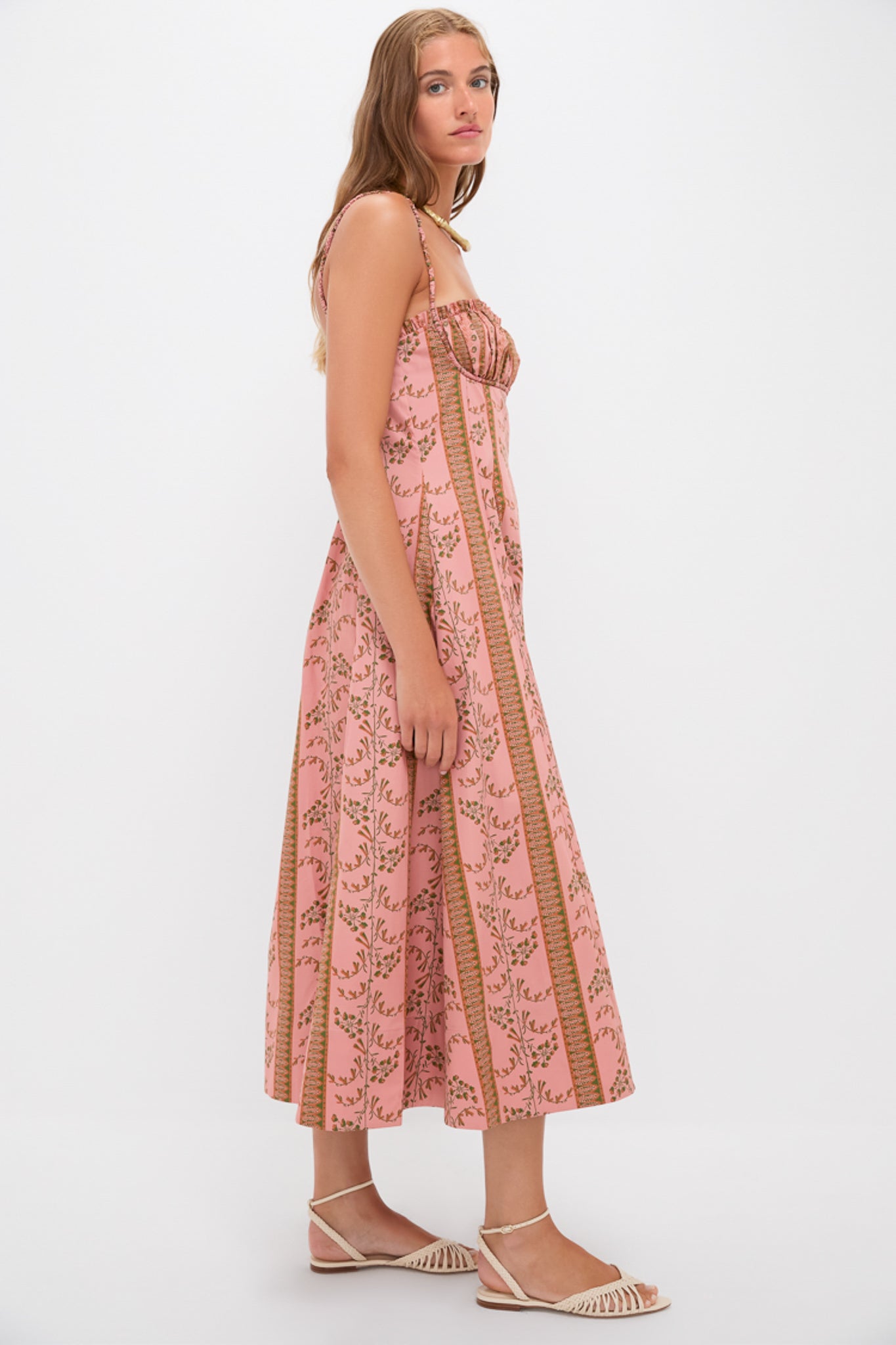 Young woman in profile wearing the Rust Dandelion Floral Stripe Maisie Dress, a classic, high-end, effortless sundress with ruched empire waist and floral motifs, styled with sandals.