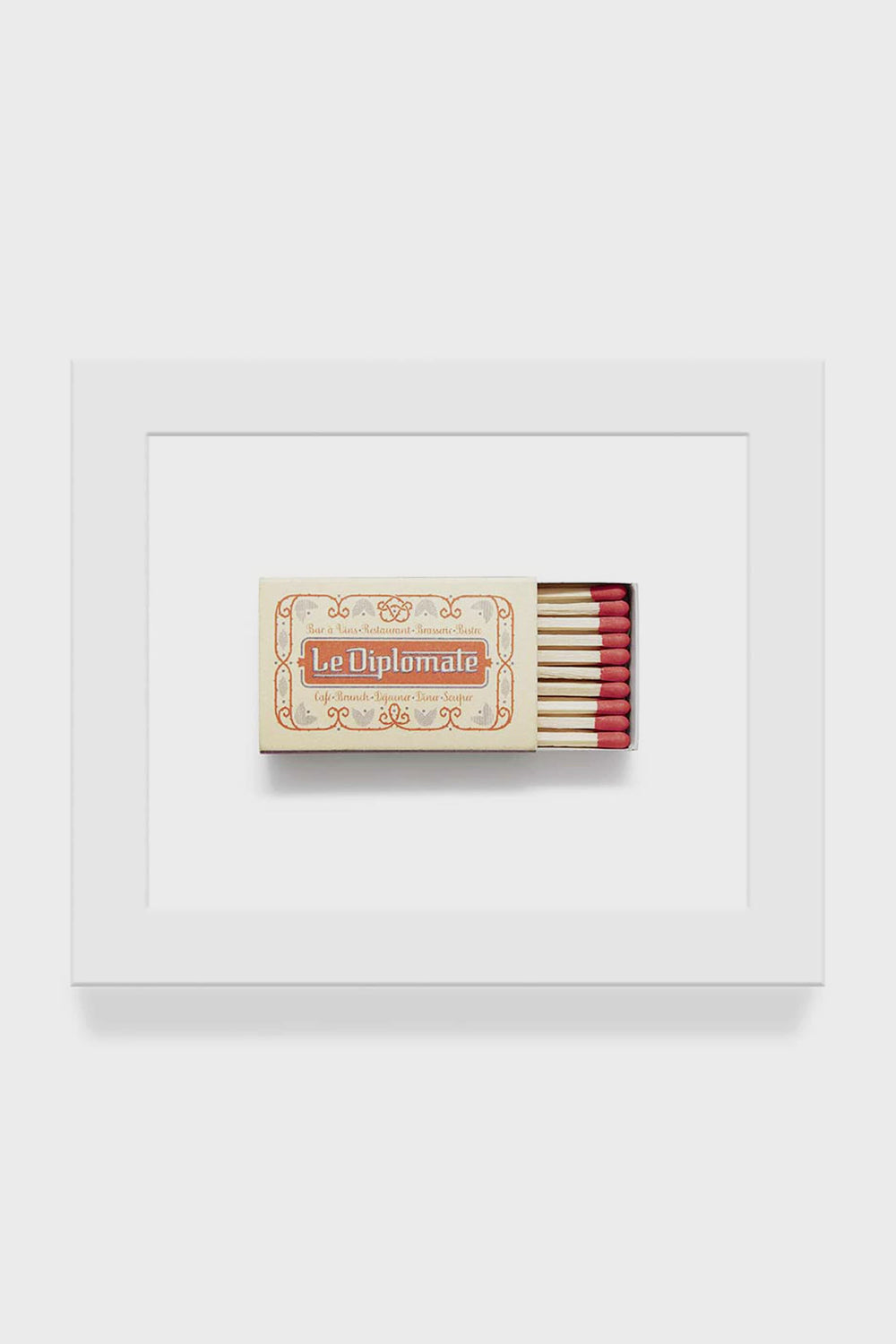 A framed macro photo of a Le Diplomate matchbox with red-tipped matches, from the Matchbook Diaries collection by Charles Ryan Clarke, displayed in a white frame.