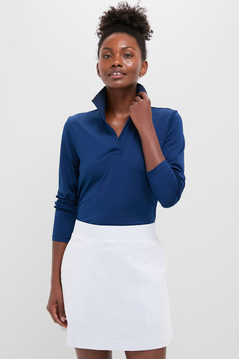 A woman stands confidently in a Tnuck Sport slim fit long sleeve polo with a popped collar, paired with a white skirt. The shirt features quick dry performance fabric for comfort and style.