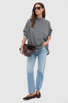 Woman models the Slate Gray Bowie Popover, an effortless, classic pullover with a swing shape and rolled neckline, paired with jeans and accessories for a high-end, fun look.